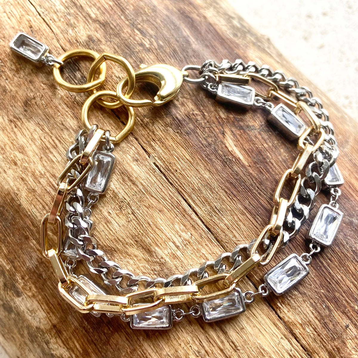 Gold and silver chain bracelet with clear gemstones on a wooden surface