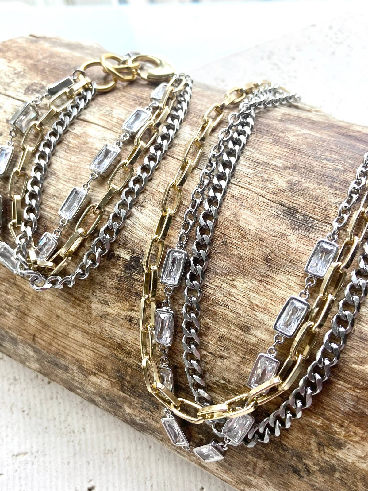 Three chain necklaces with clear gemstones on a wooden surface
