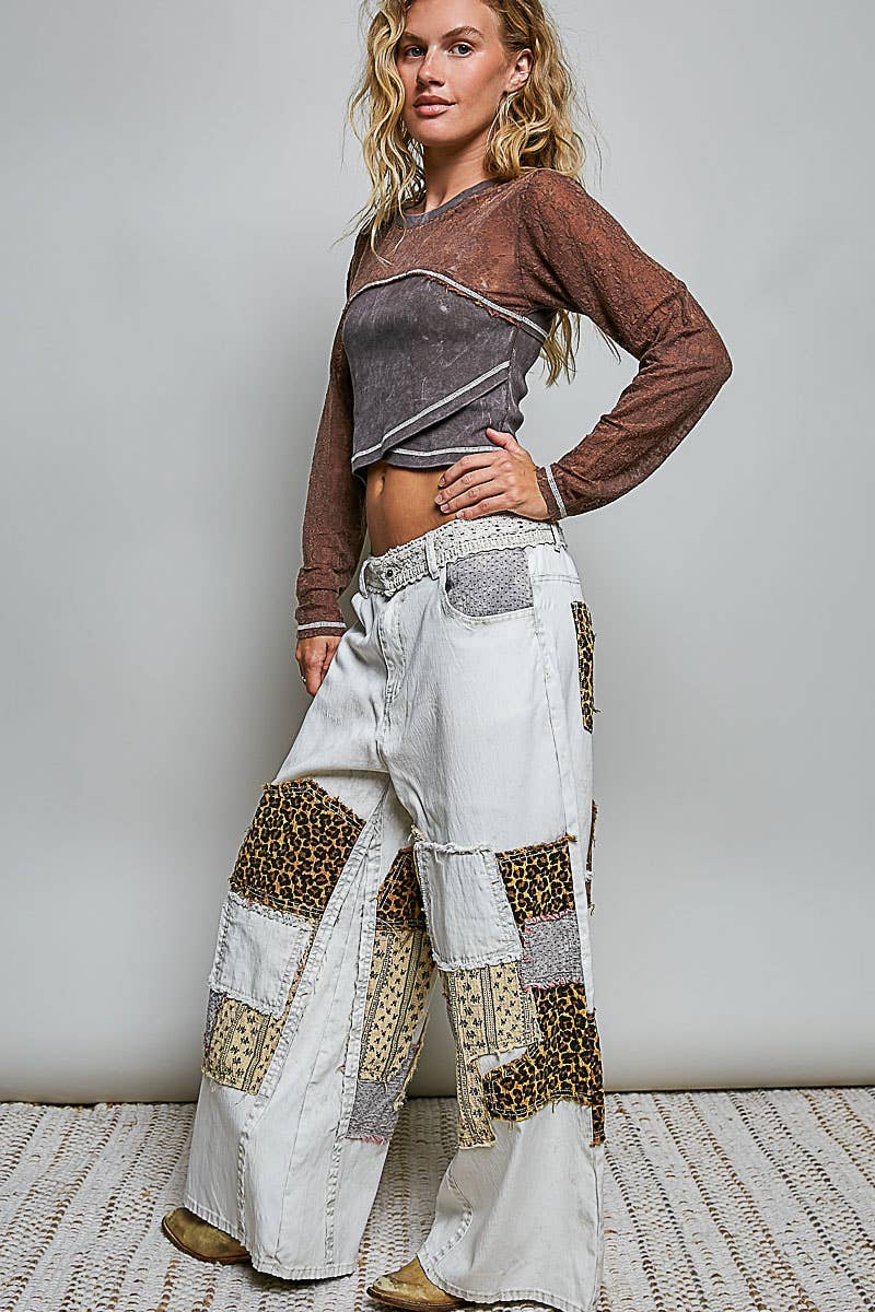 Woman wearing a brown long-sleeve top and white patchwork pants against a plain background
