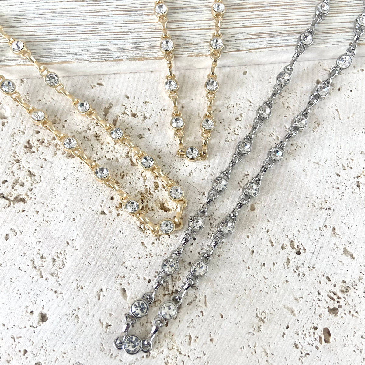 Two necklaces, one gold and one silver, on a textured surface.
