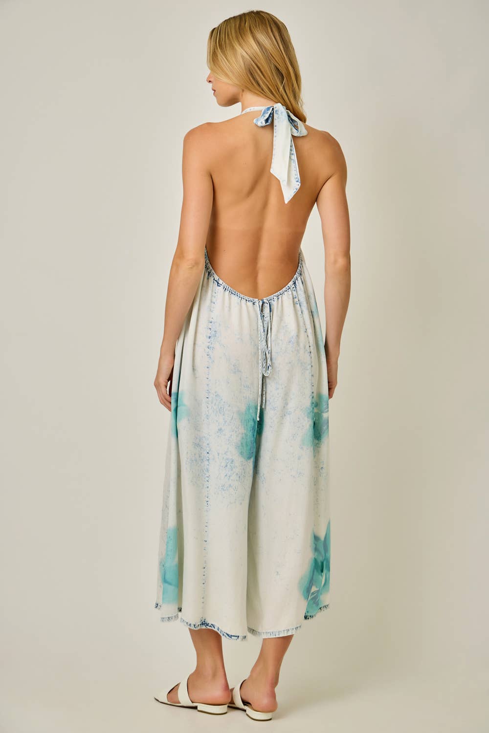 Woman wearing a floral jumpsuit with a halter neck design on a plain background