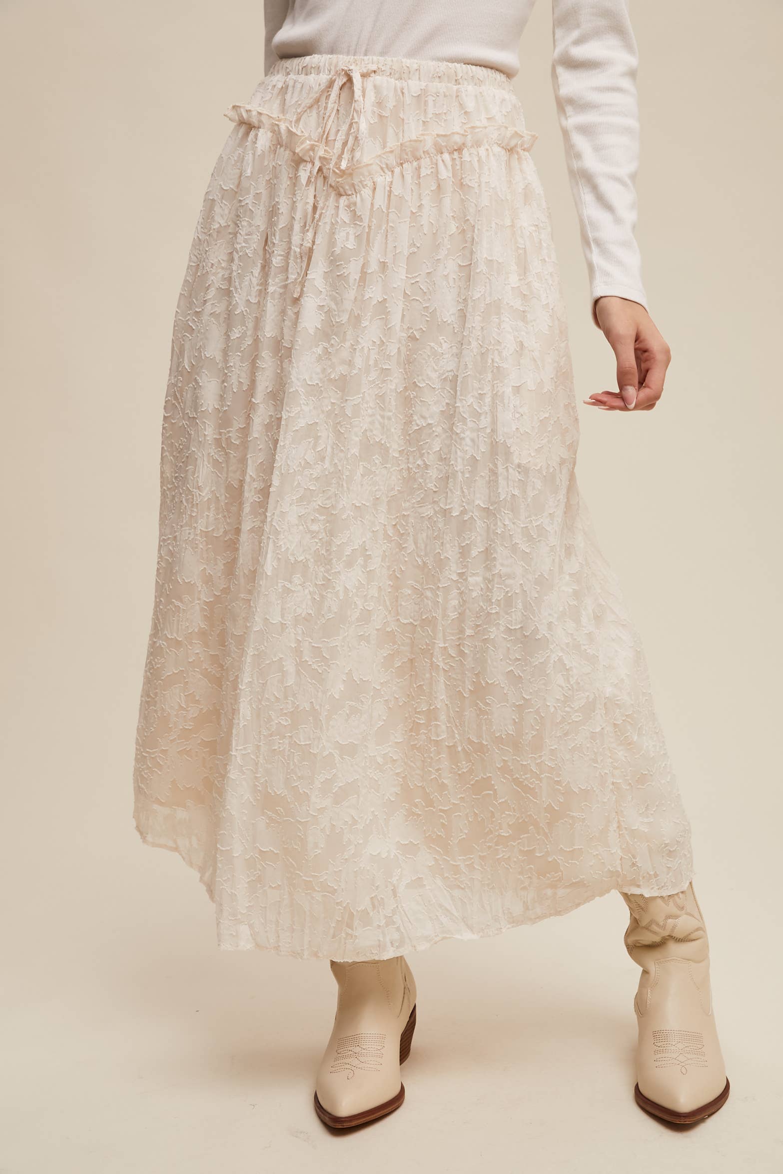 Ivory floral lace maxi skirt with elastic drawstring waist and ruffle detail, ankle-length bubble hem; shown on model with cream western boots.