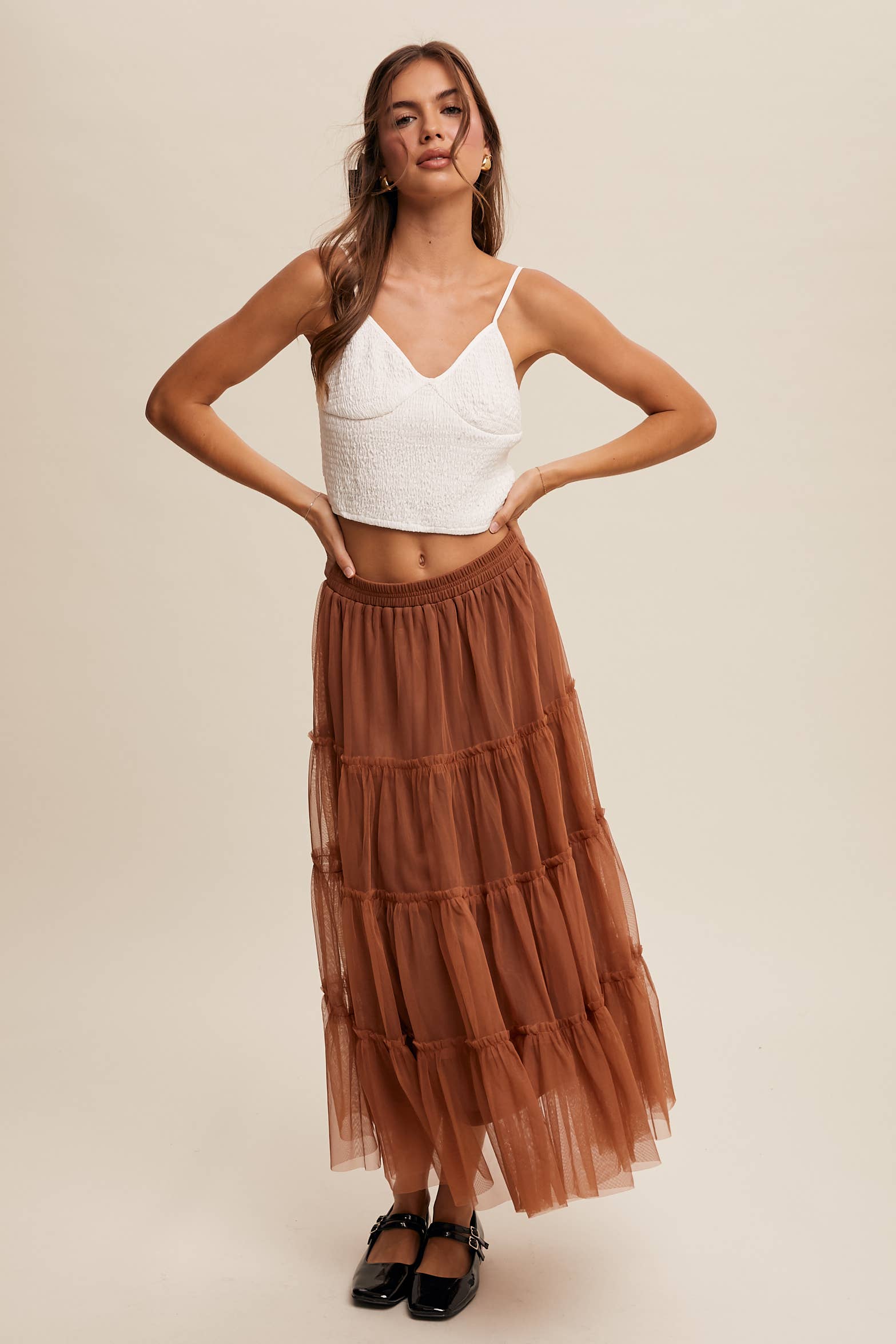 Front view — rust tulle tiered midi skirt with elastic waist and ruffle tiers, sheer overlay; model in black Mary Jane flats.
