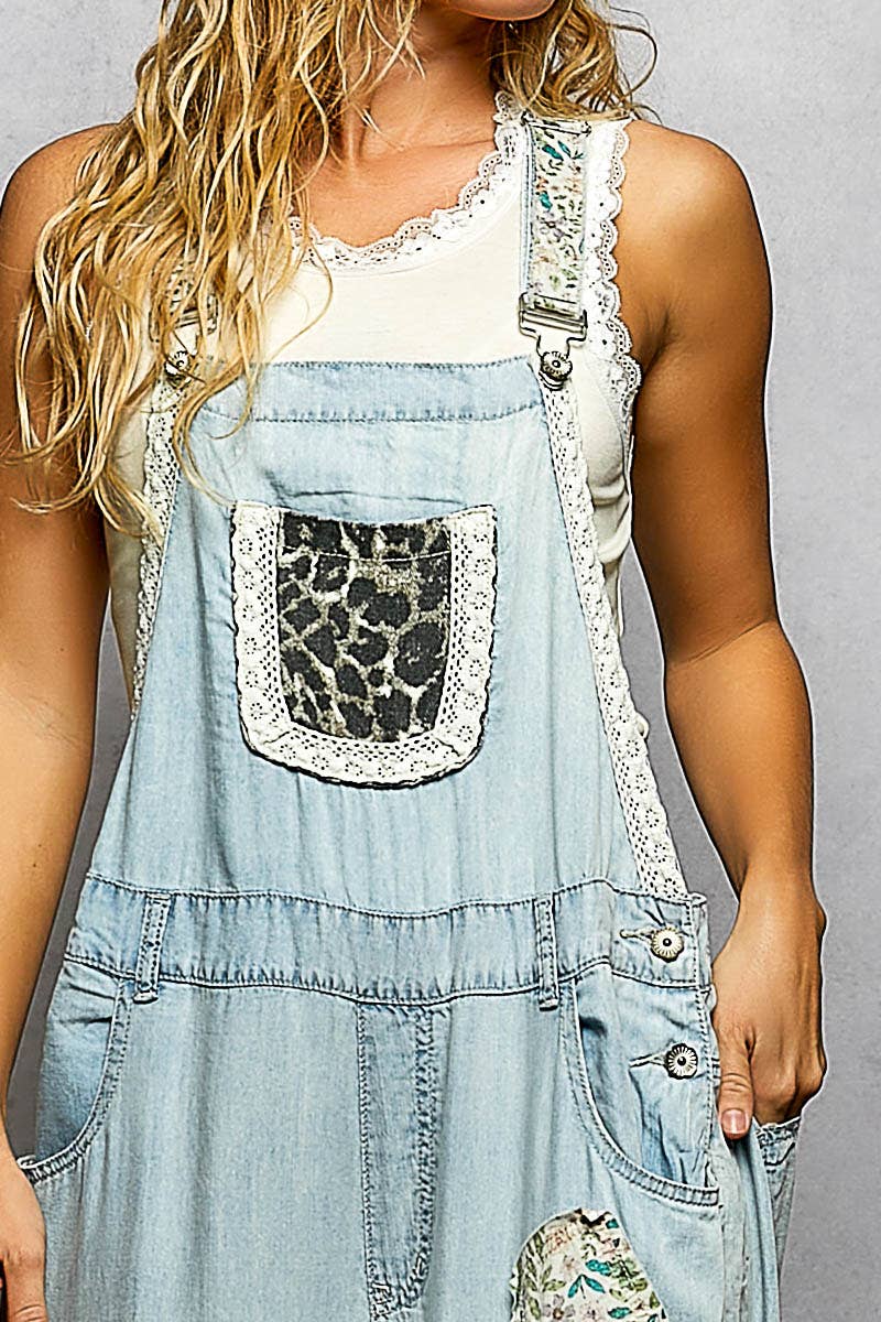 Close-up of mixed print ruffle wide leg overall bib — leopard print pocket with lace trim, printed fabric strap with hardware, light wash denim bodice detail