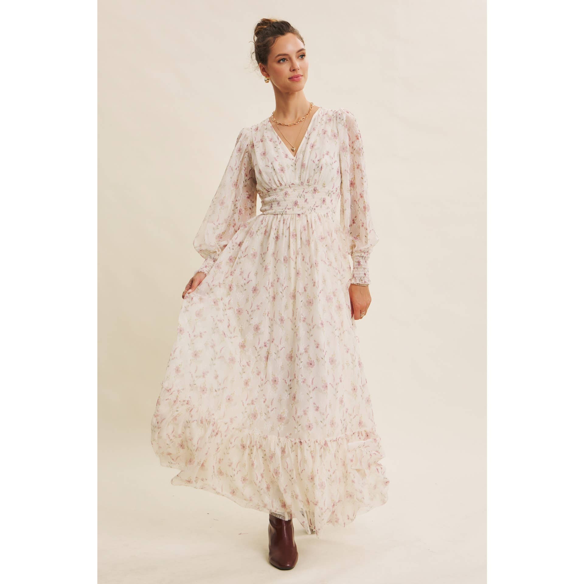 Front view — cream floral chiffon maxi dress with V-neck, sheer long sleeves, smocked waist, and ruffle hem; styled with brown boots.