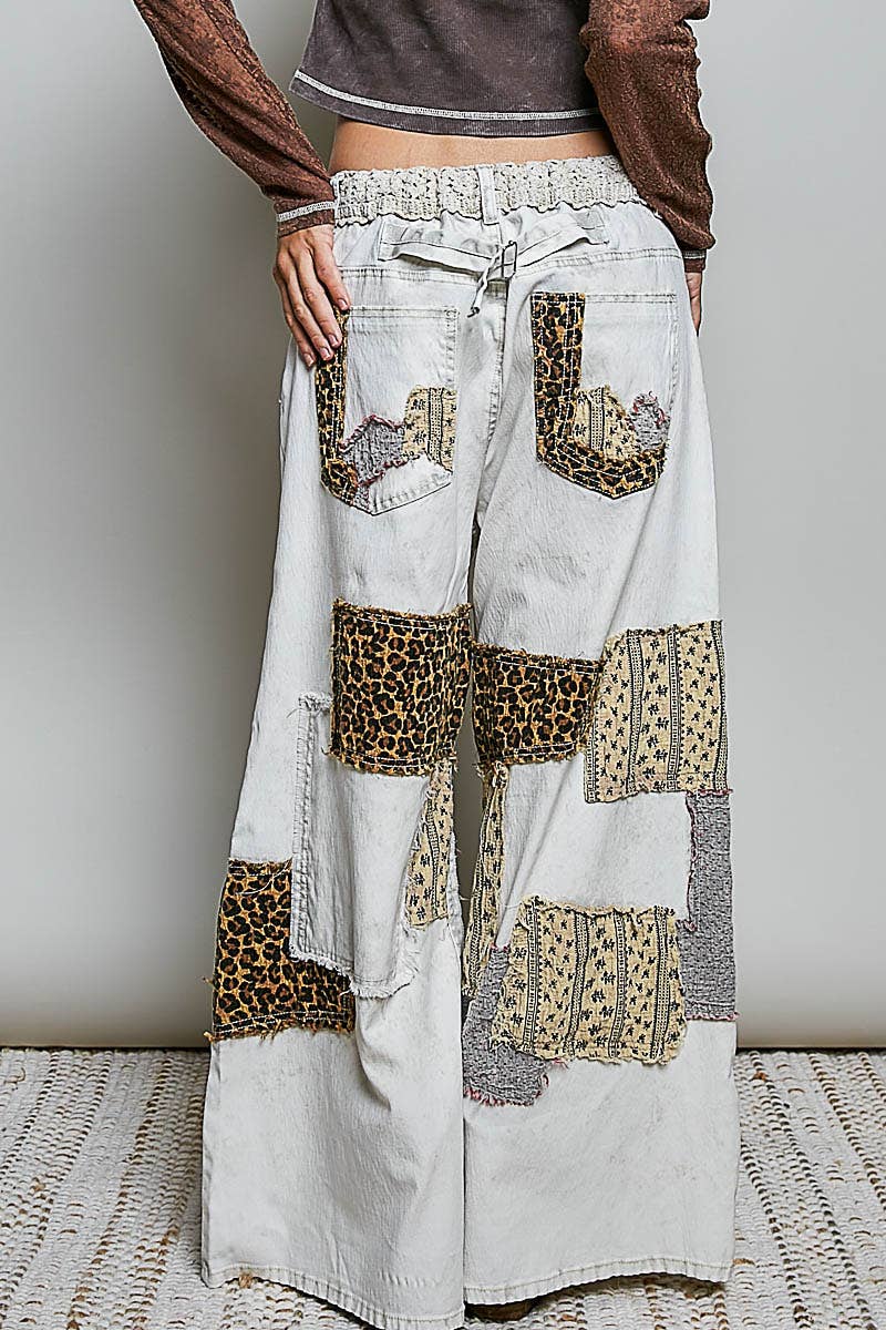 Long white denim pants with leopard print patches worn by a person against a neutral background
