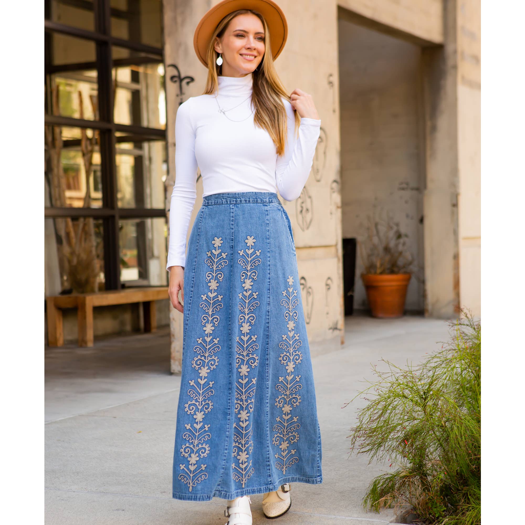 Woman wearing a white top and blue embroidered skirt outdoors.