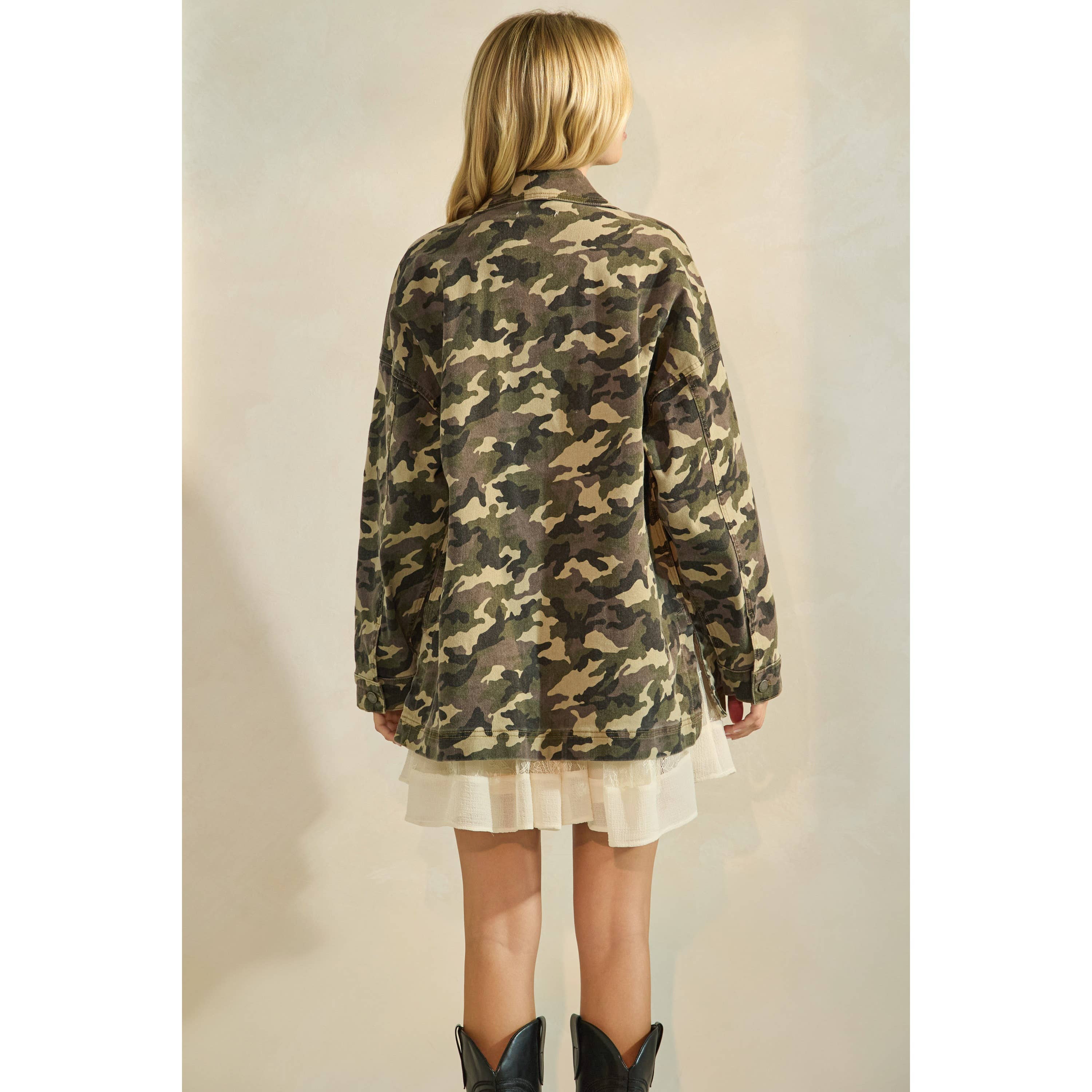 Back view of oversized camouflage print jacket with front pockets and button closure, styled over a white tiered mini dress and black western boots.