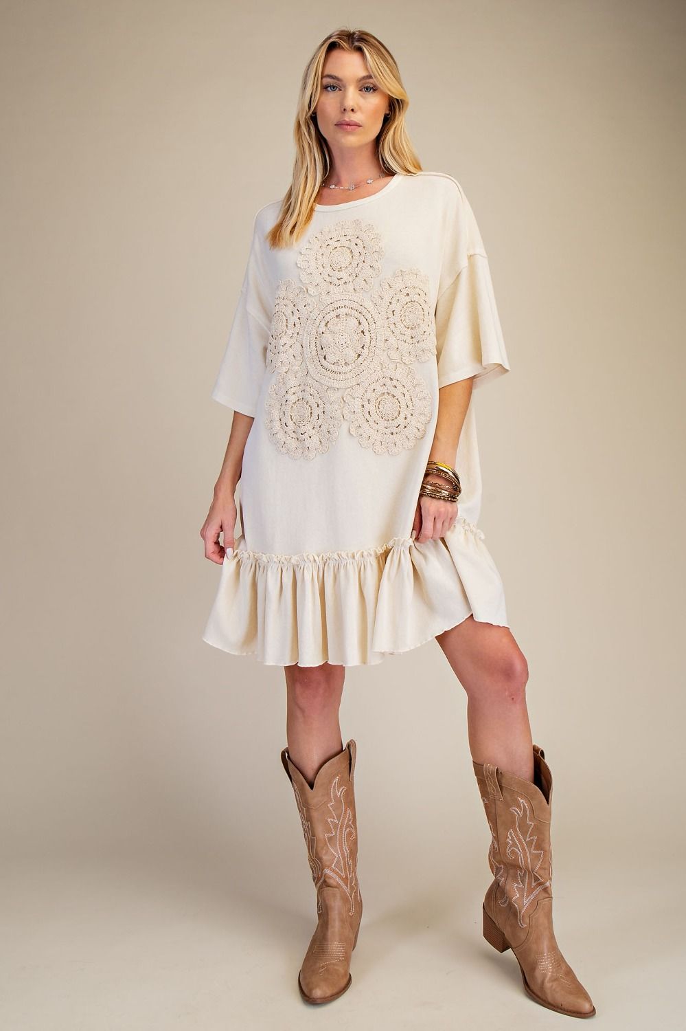 Woman wearing a white dress with intricate patterns and brown cowboy boots on a beige background