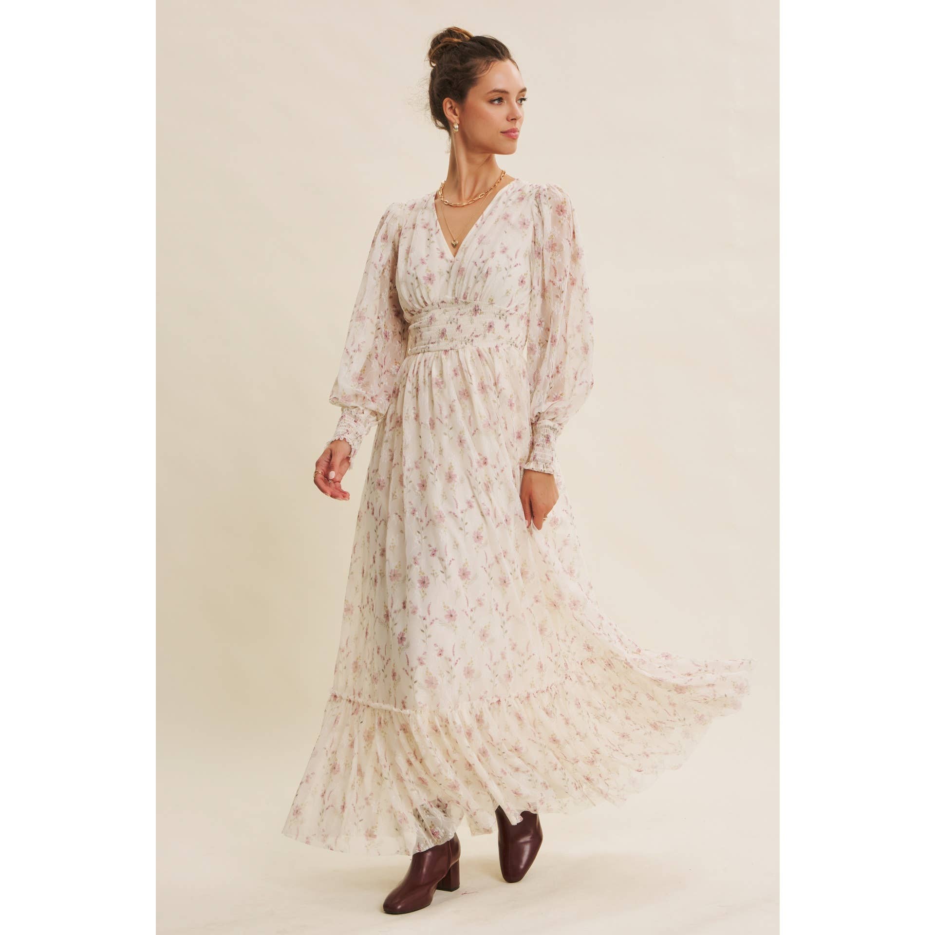 Front view — cream floral chiffon maxi dress with V-neck, sheer long sleeves, smocked waist, and ruffle hem; styled with brown boots.