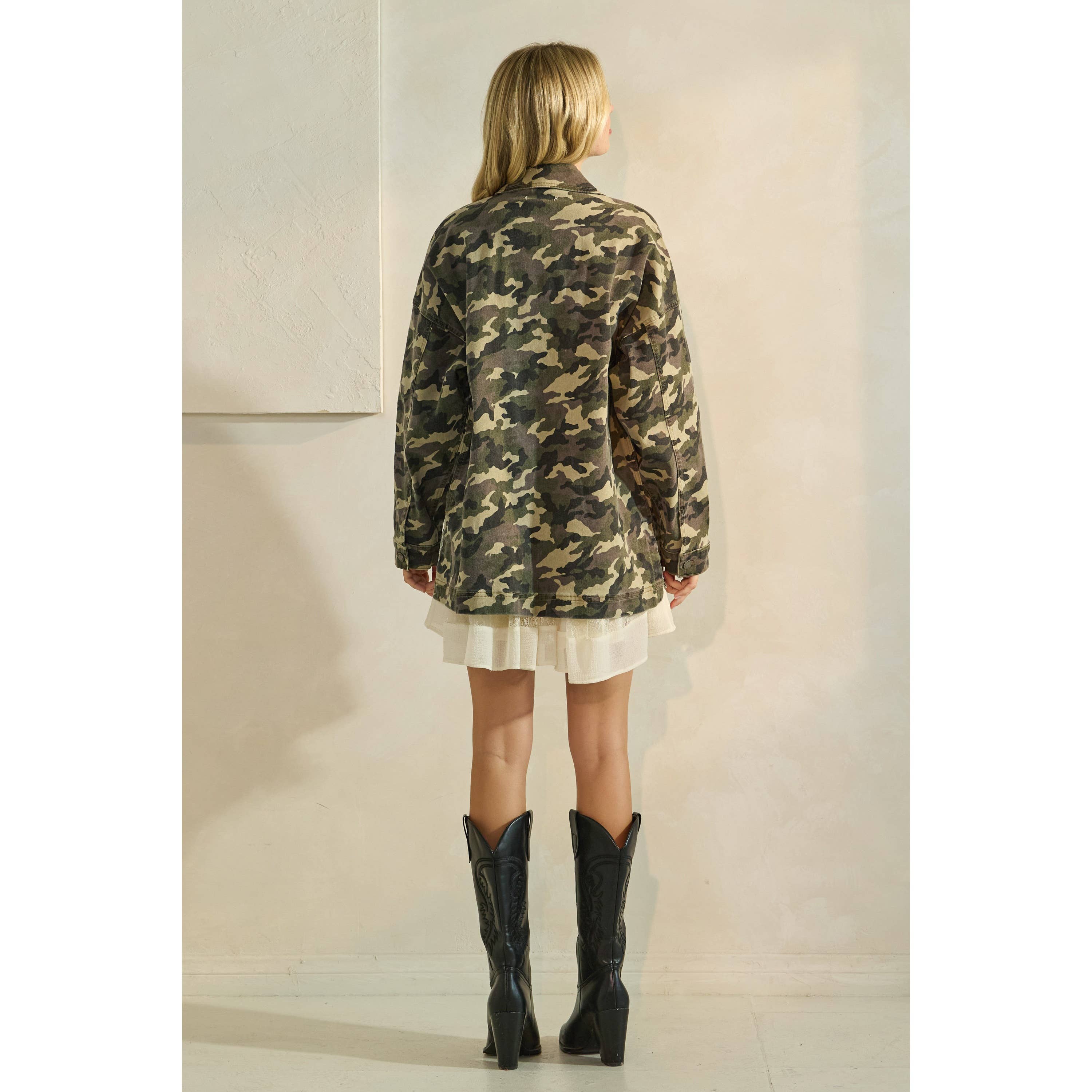 Oversized camouflage print jacket with front pockets and button closure, styled over a white tiered mini dress.