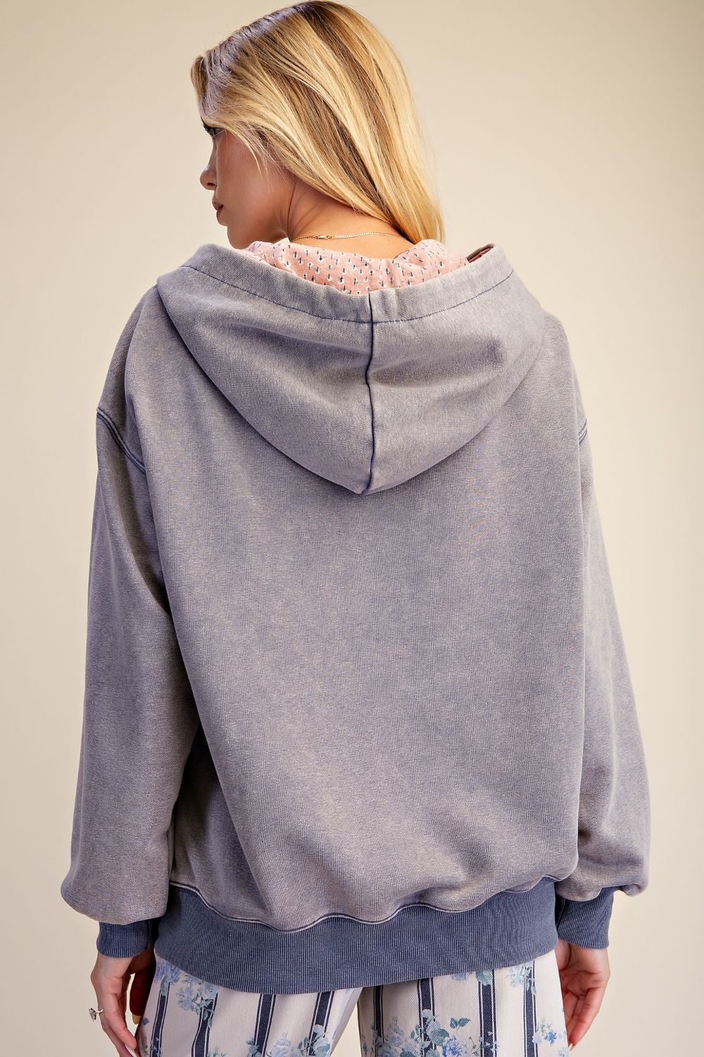 Back view of woman wearing slate blue mineral wash oversized hoodie, showing relaxed dropped-shoulder silhouette and contrast-printed hood lining peeking out