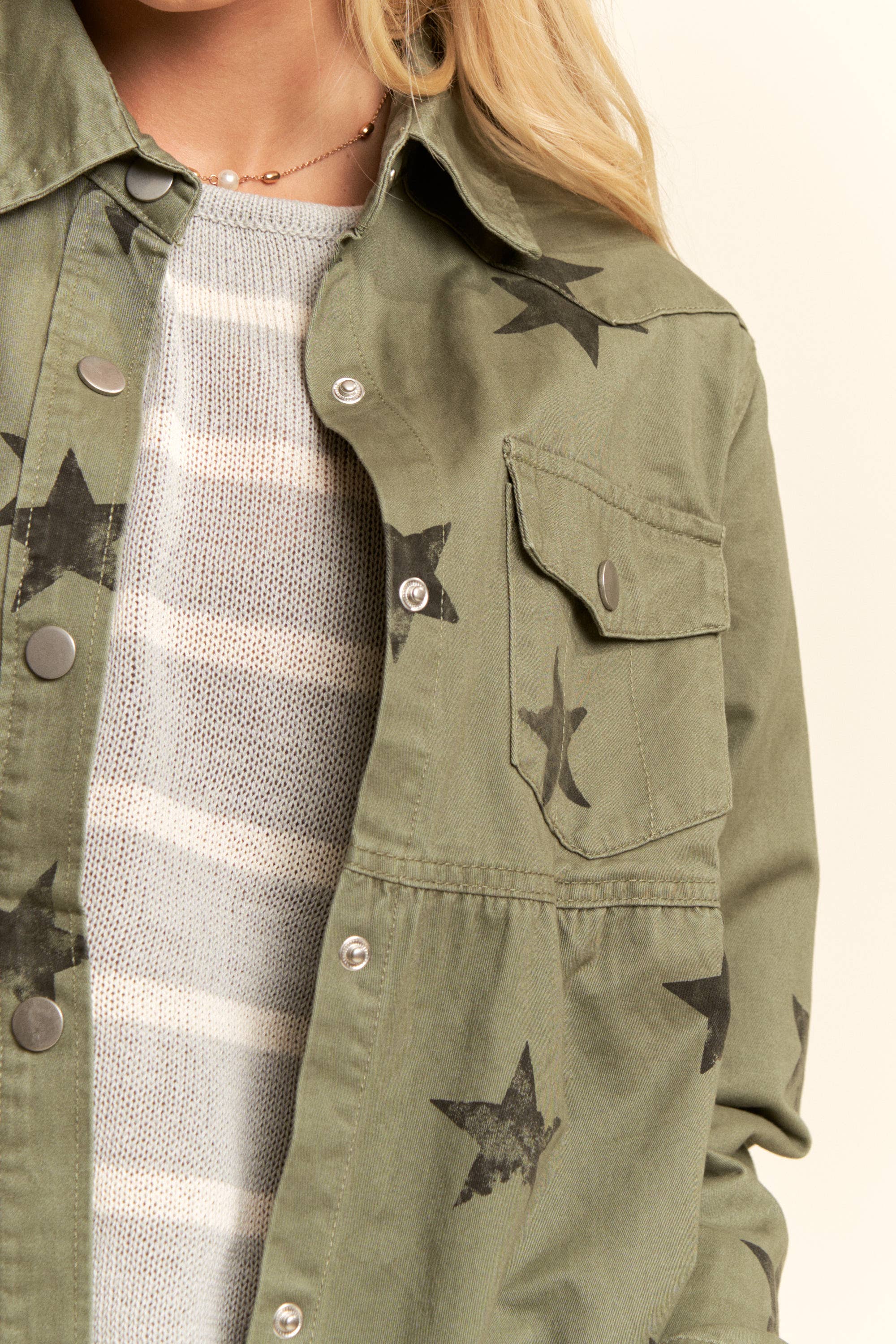 Up close- Olive star-print babydoll shacket with snap-button front, chest flap pockets, dropped shoulders, relaxed fit, and frayed curved hem.