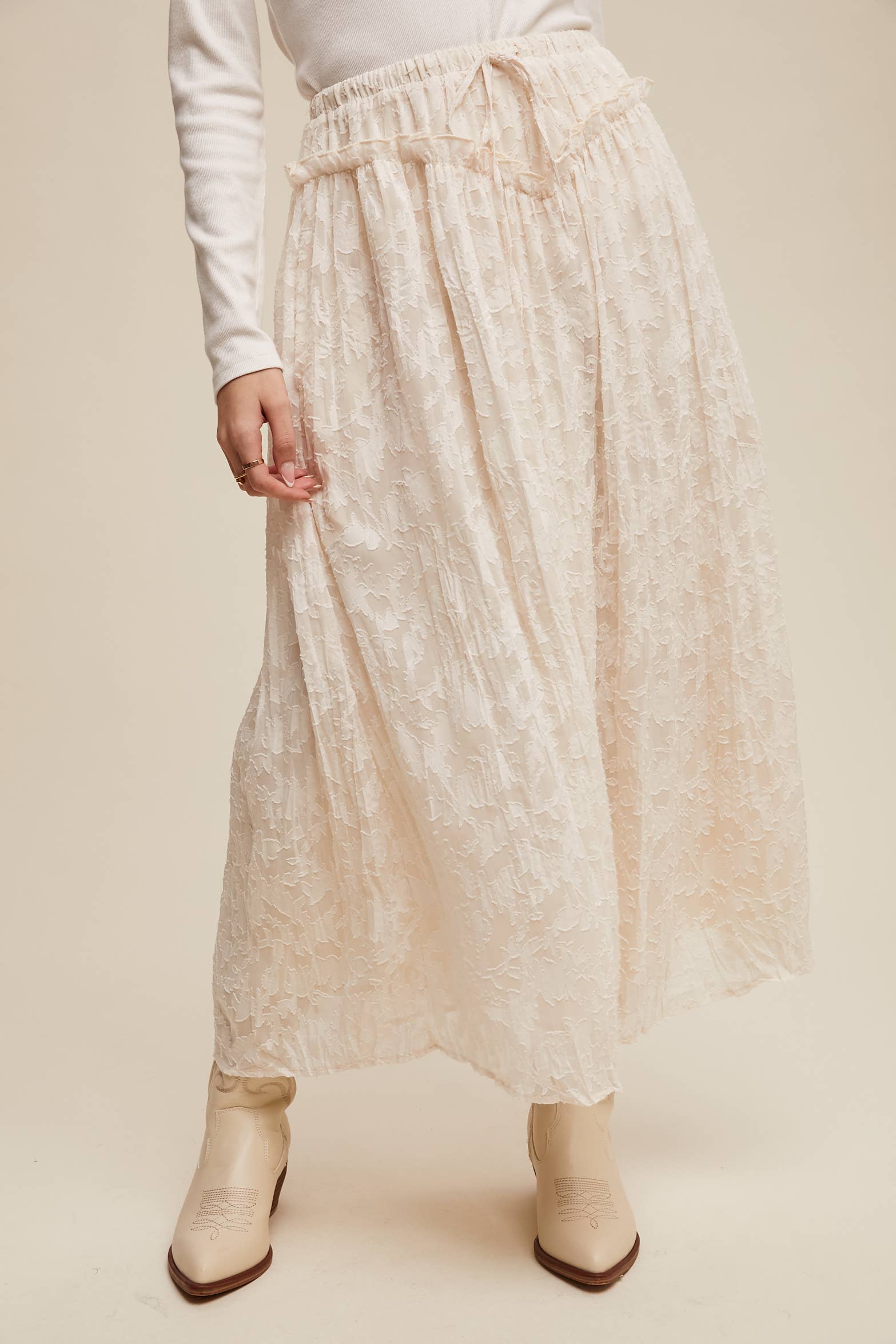 Ivory floral lace maxi skirt with elastic drawstring waist and ruffle detail, ankle-length bubble hem; shown on model with cream western boots.