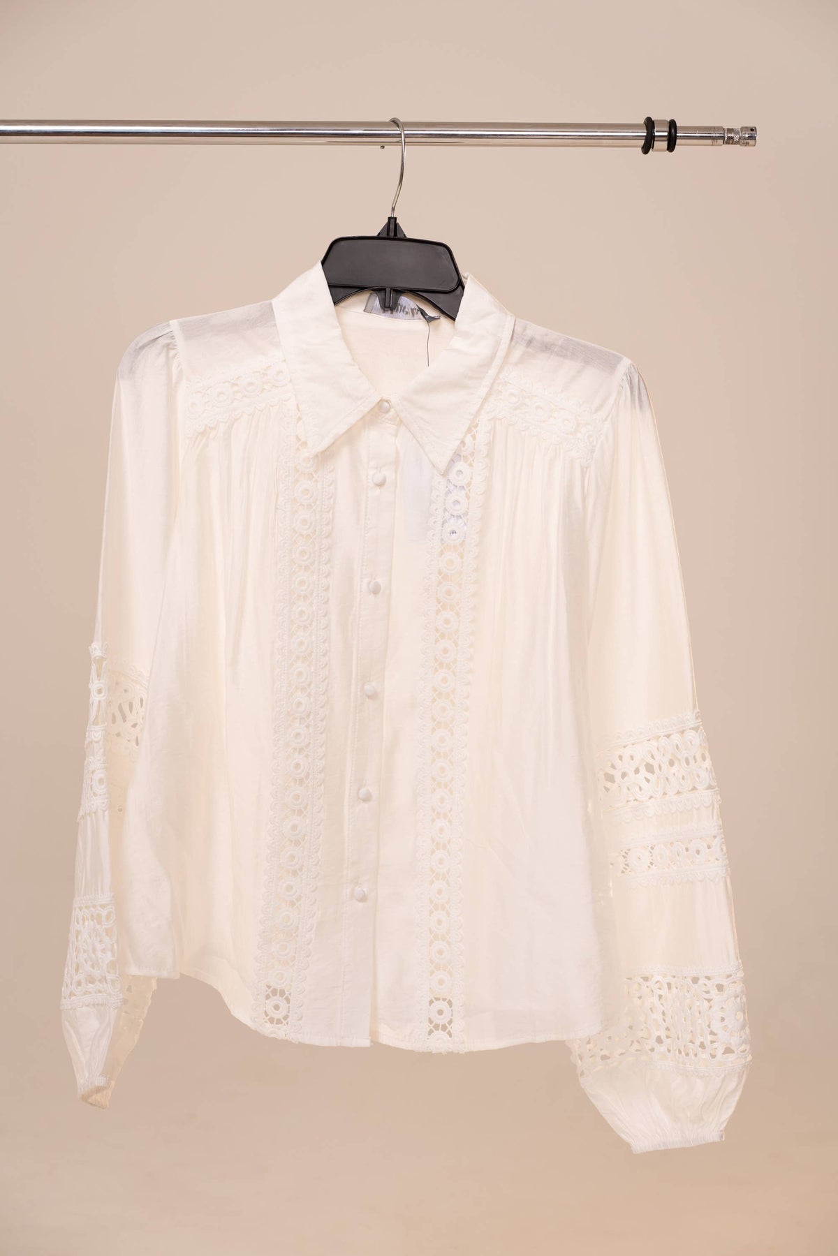 White lace blouse on a hanger against a beige background