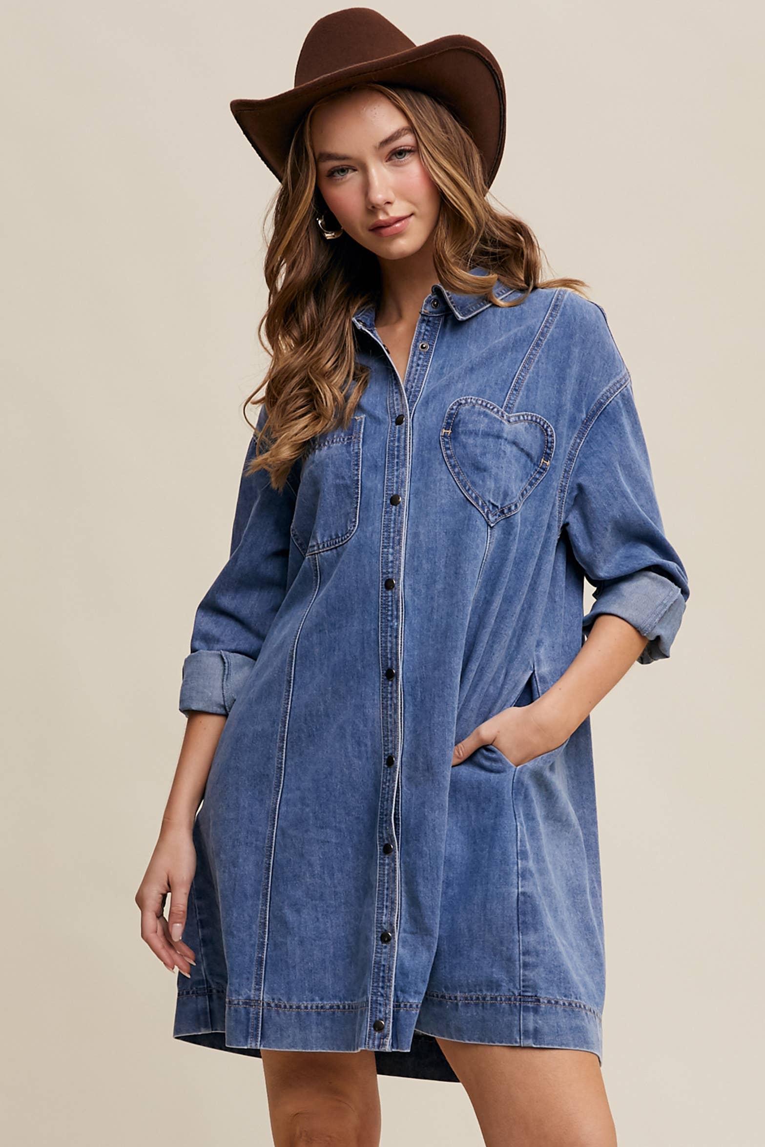 Medium-wash denim shirt dress with snap button front, heart-shaped chest pocket, rolled long sleeves, and a relaxed mini silhouette.