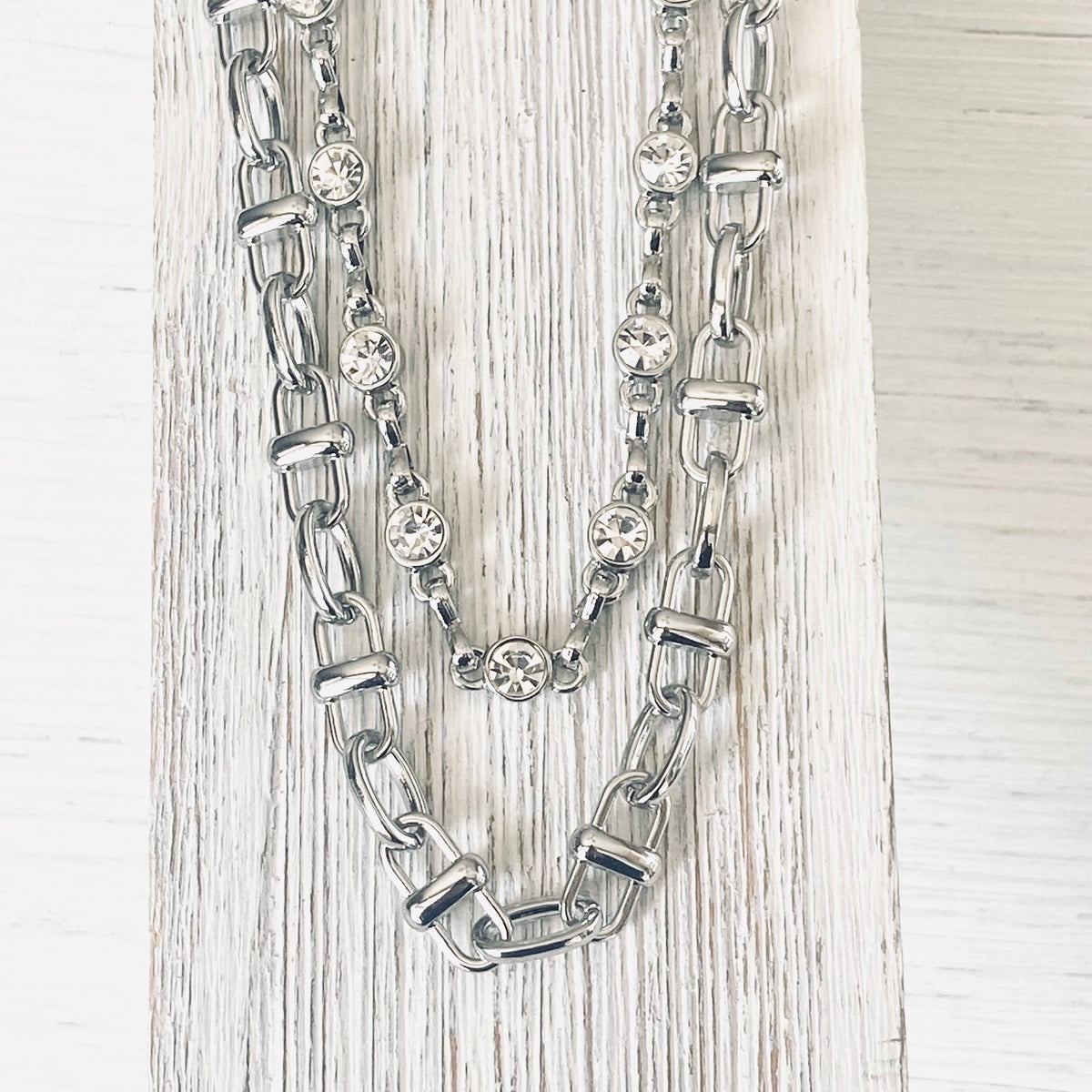 Silver chain necklace with embedded crystals on a light wooden surface