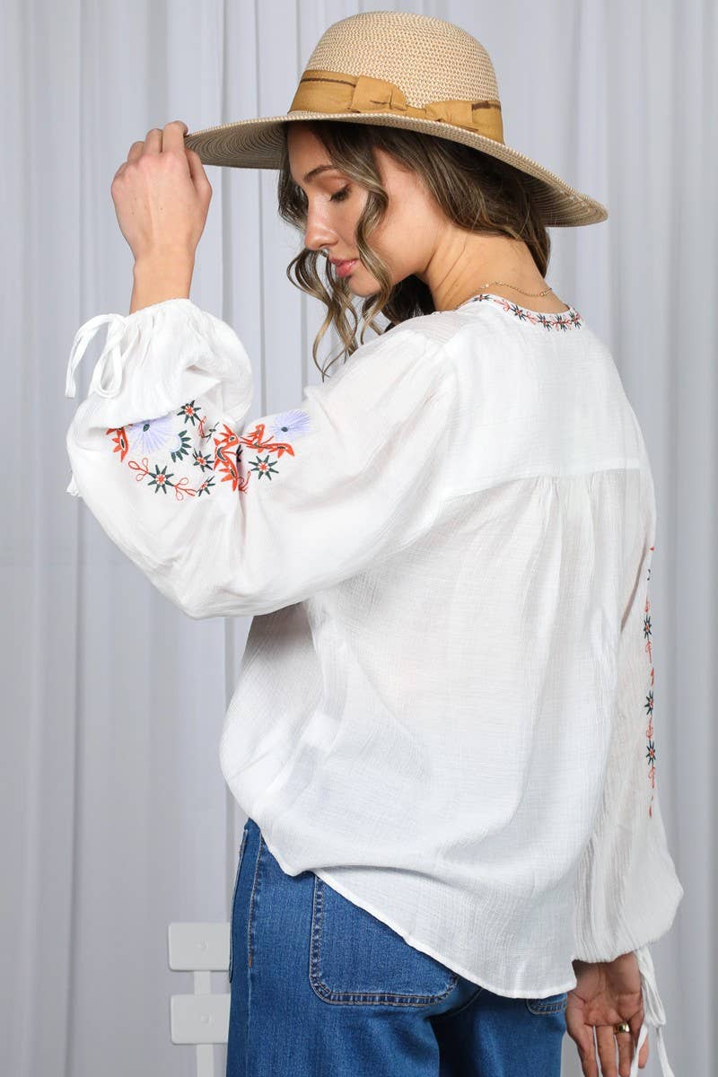 White embroidered peasant blouse with multicolor floral front, split V-neck, and balloon sleeves with ties