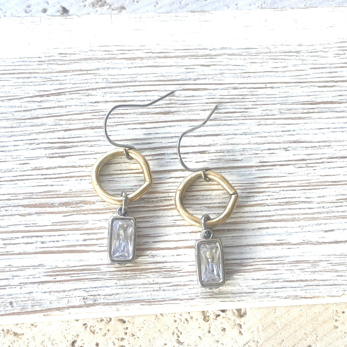 Pair of earrings with gold and silver rings and clear gemstones on a textured surface