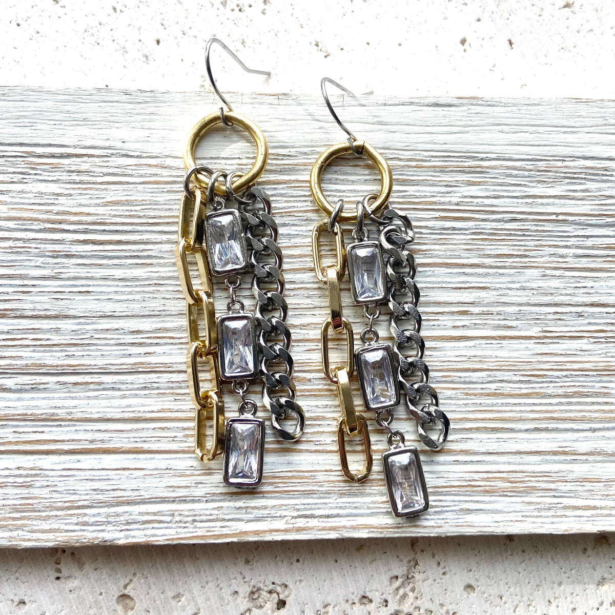Pair of earrings with chain and crystal-like elements on a textured surface