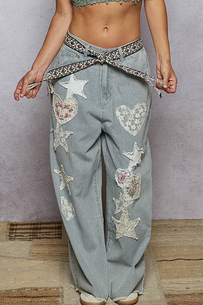 Close-up of a woven black and beige boho belt with stud accents and tassel ends, styled around striped denim jeans with lace patches.