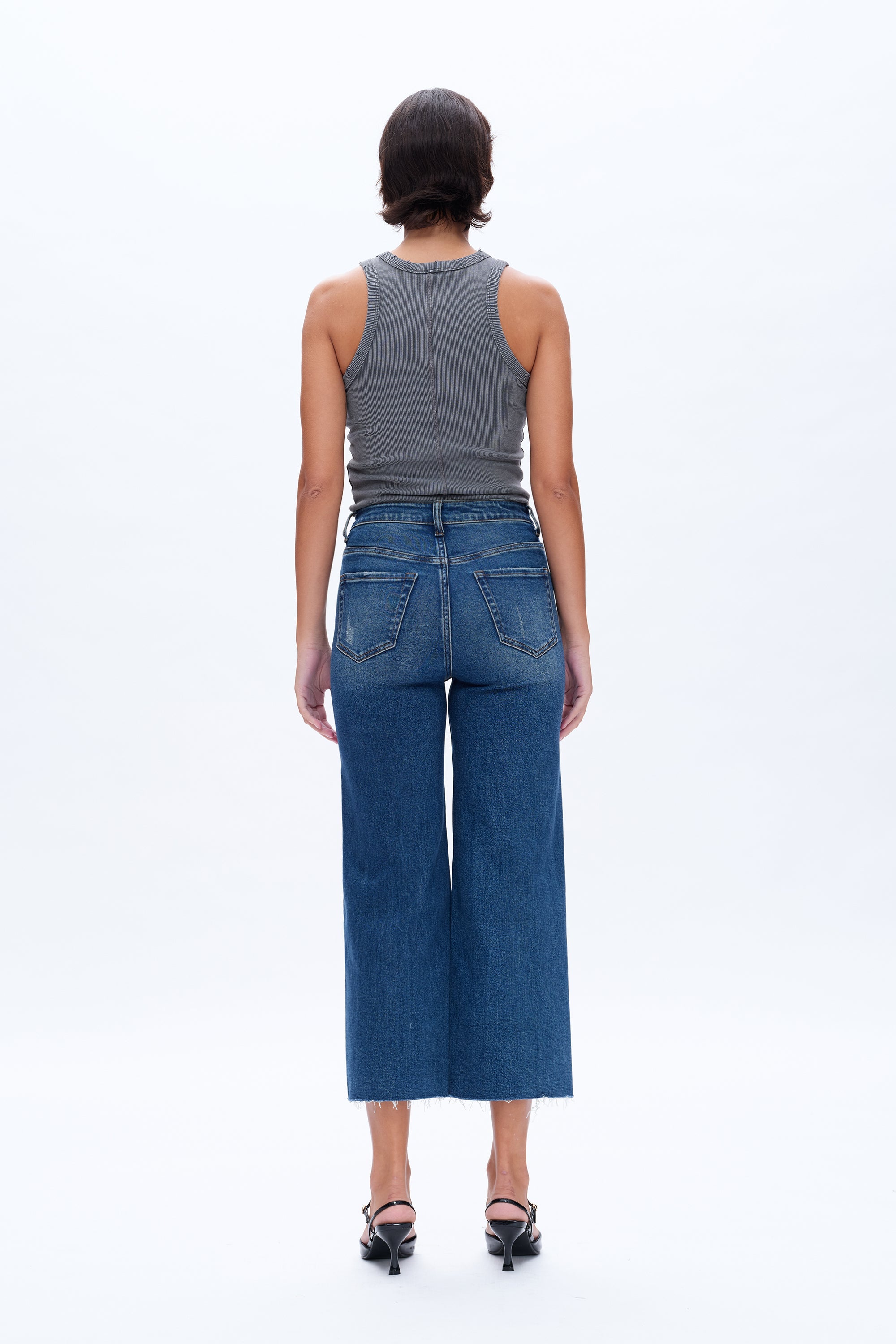 Person wearing a gray tank top and blue jeans on a white background