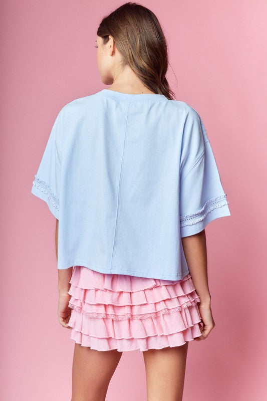 Light blue oversized tee with bow-wrapped football graphic and lace-trim sleeves, styled with a pink tiered ruffle mini skirt.