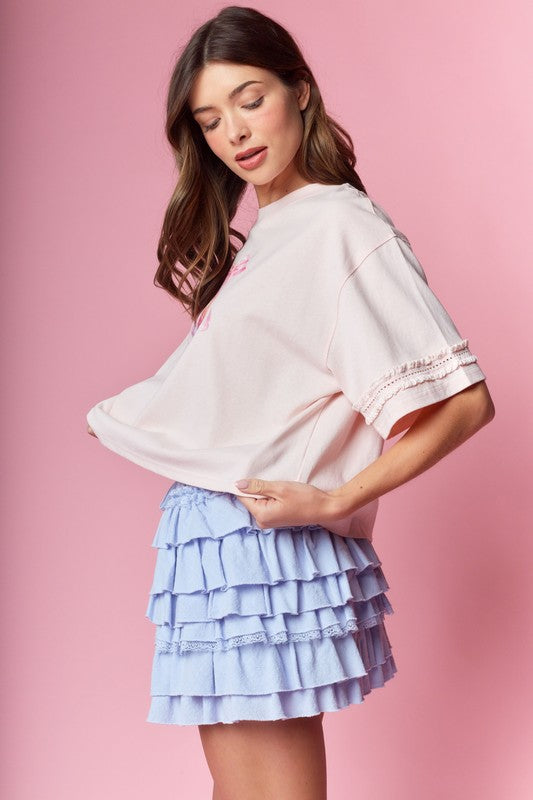 Blush pink oversized tee with lace-trimmed elbow sleeves shown from the side, paired with a periwinkle tiered ruffle mini skirt.