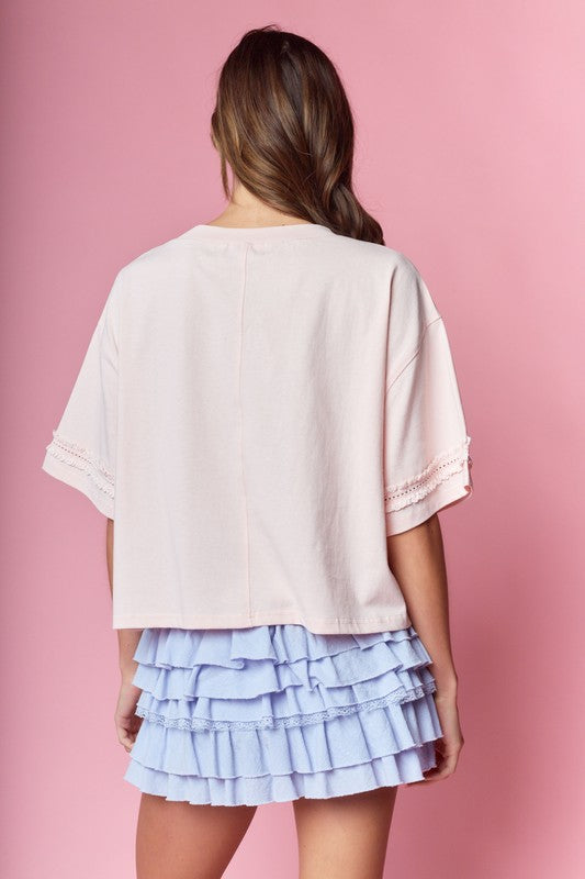 Blush pink oversized tee with lace-trimmed elbow sleeves shown from the side, paired with a periwinkle tiered ruffle mini skirt.
