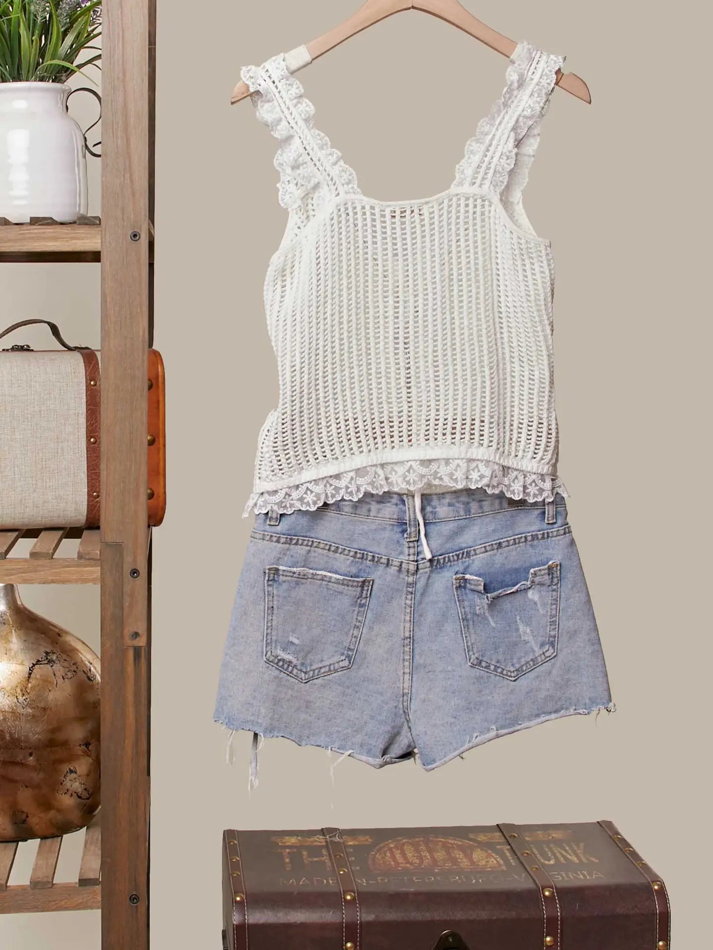 White lace top and denim shorts on a hanger against a neutral background