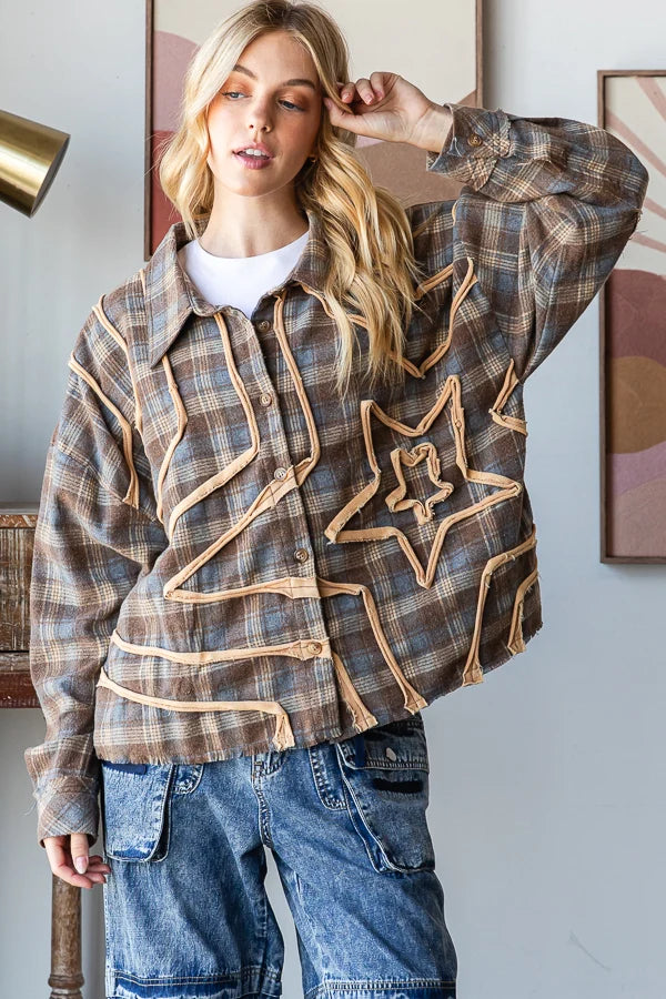 A woman wearing a brown and beige plaid button-up shirt jacket with a large star applique on the front, styled with blue jeans and a white t-shirt, in an indoor setting.