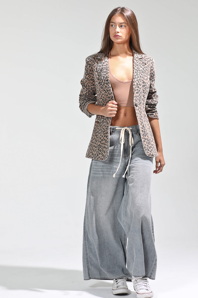 Woman wearing a leopard print blazer, pink top, and gray wide-leg pants on a white background