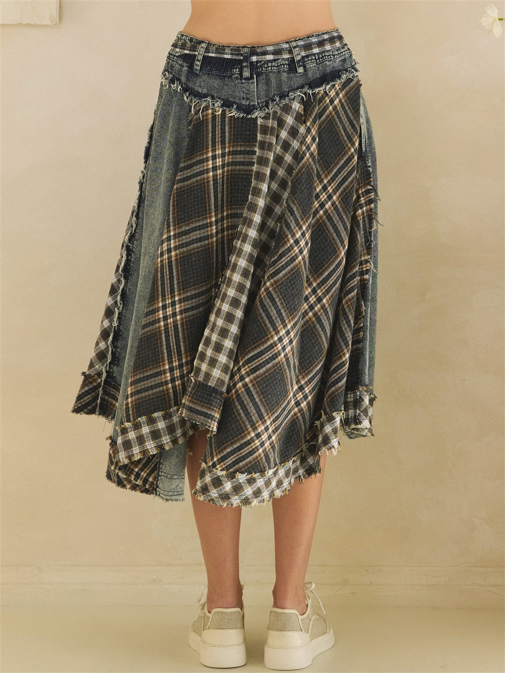 Close-up of the denim waistband and layered plaid panels on an asymmetrical draped skirt.
