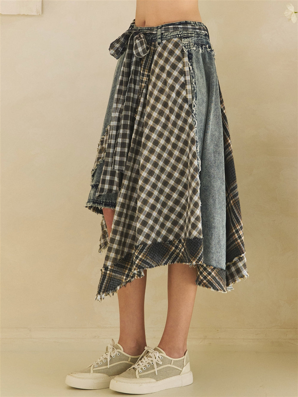 Model wearing a blue denim and plaid mixed skirt styled with a fitted top and sneakers side view 