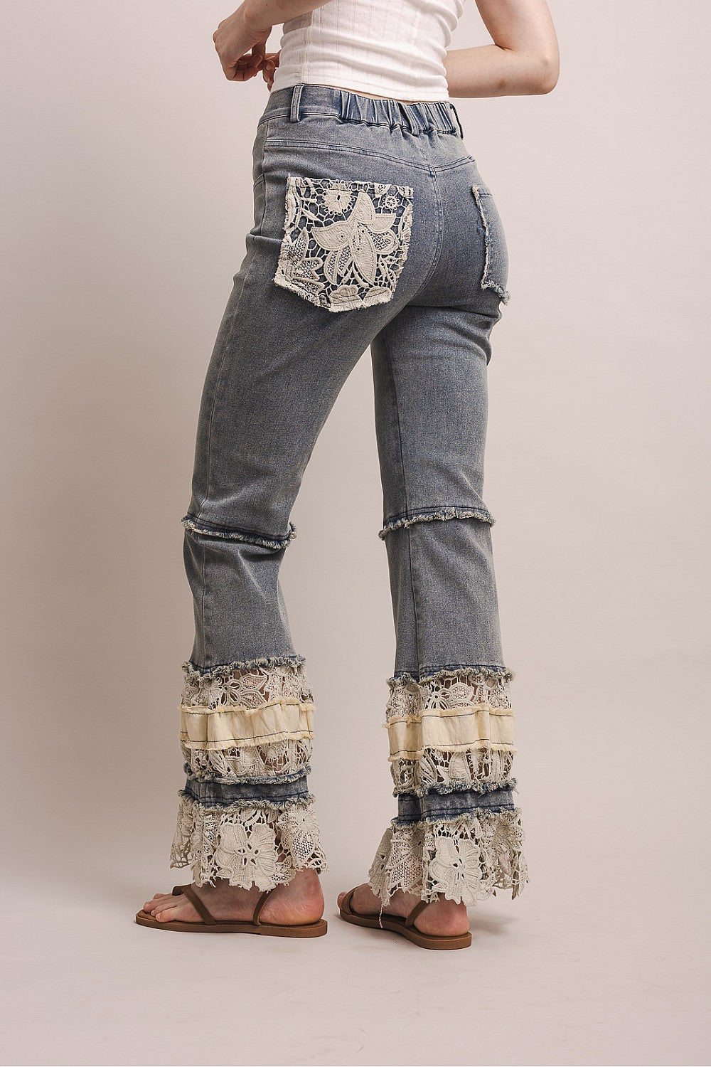 Blue jeans with lace detailing on cuffs and pockets against a plain background